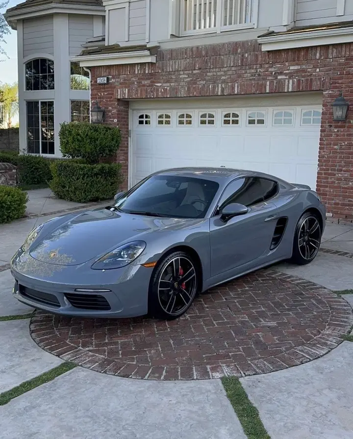 Grey Porsche 718 Cayman detailed in a brick driveway in front of a white garage