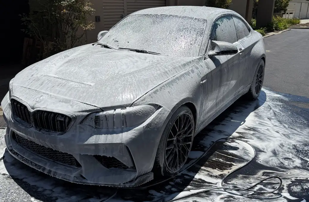 A grey BMW covered in foam during a maintenance wash in a driveway